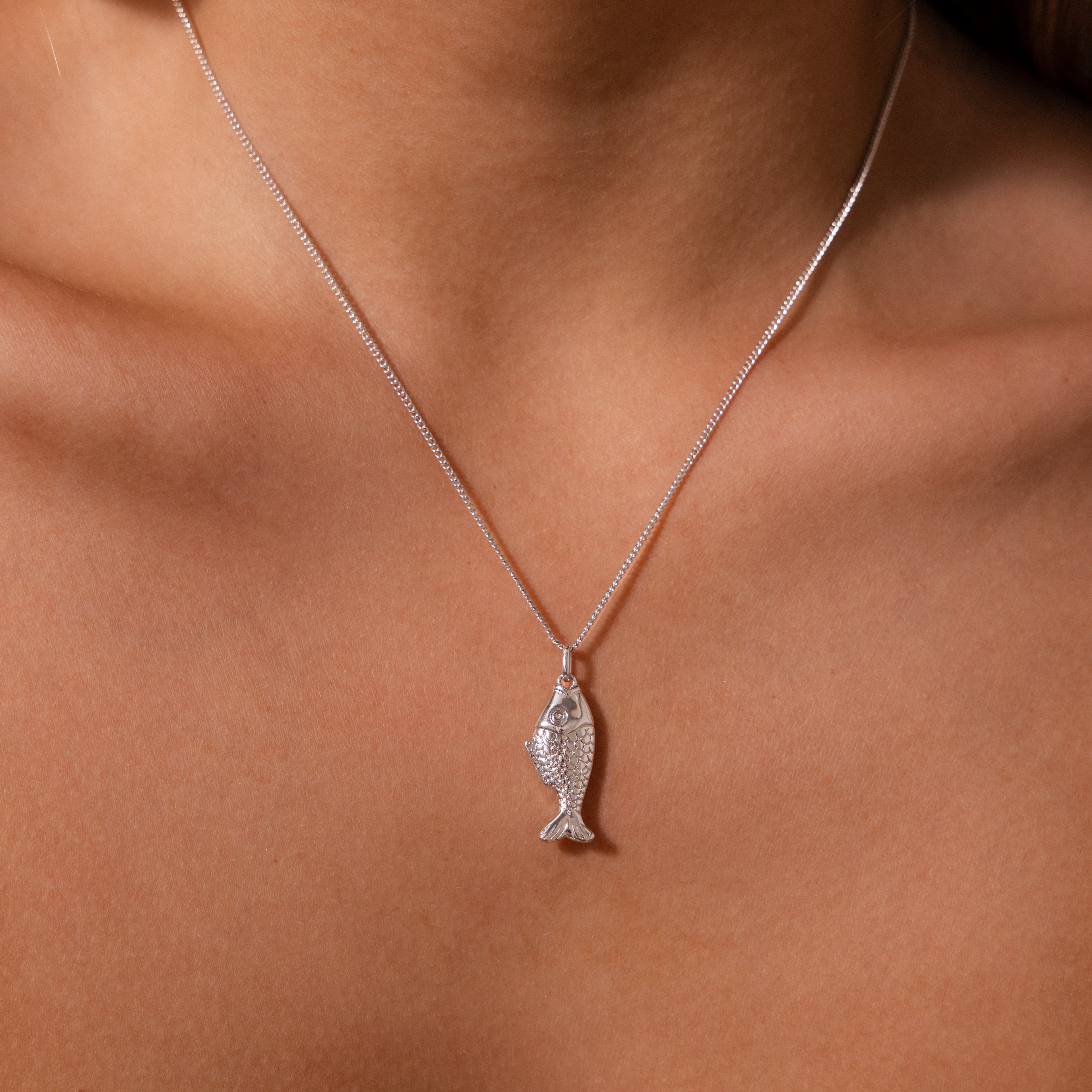 The Fish Pendant Necklace in Silver, inspired by the ocean and elegantly designed, rests on bare skin—a perfect accessory for effortless layering with any style.