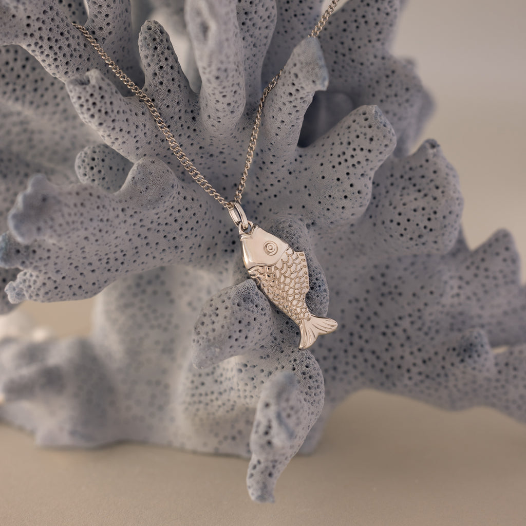 Fish Pendant Necklace in Silver, shown on textured light gray coral—perfect for layering and adding a coastal touch to any look.