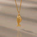 The Fish Pendant Necklace features an ocean-inspired design on a gold chain, perfect for layering and shown against a soft, neutral background.