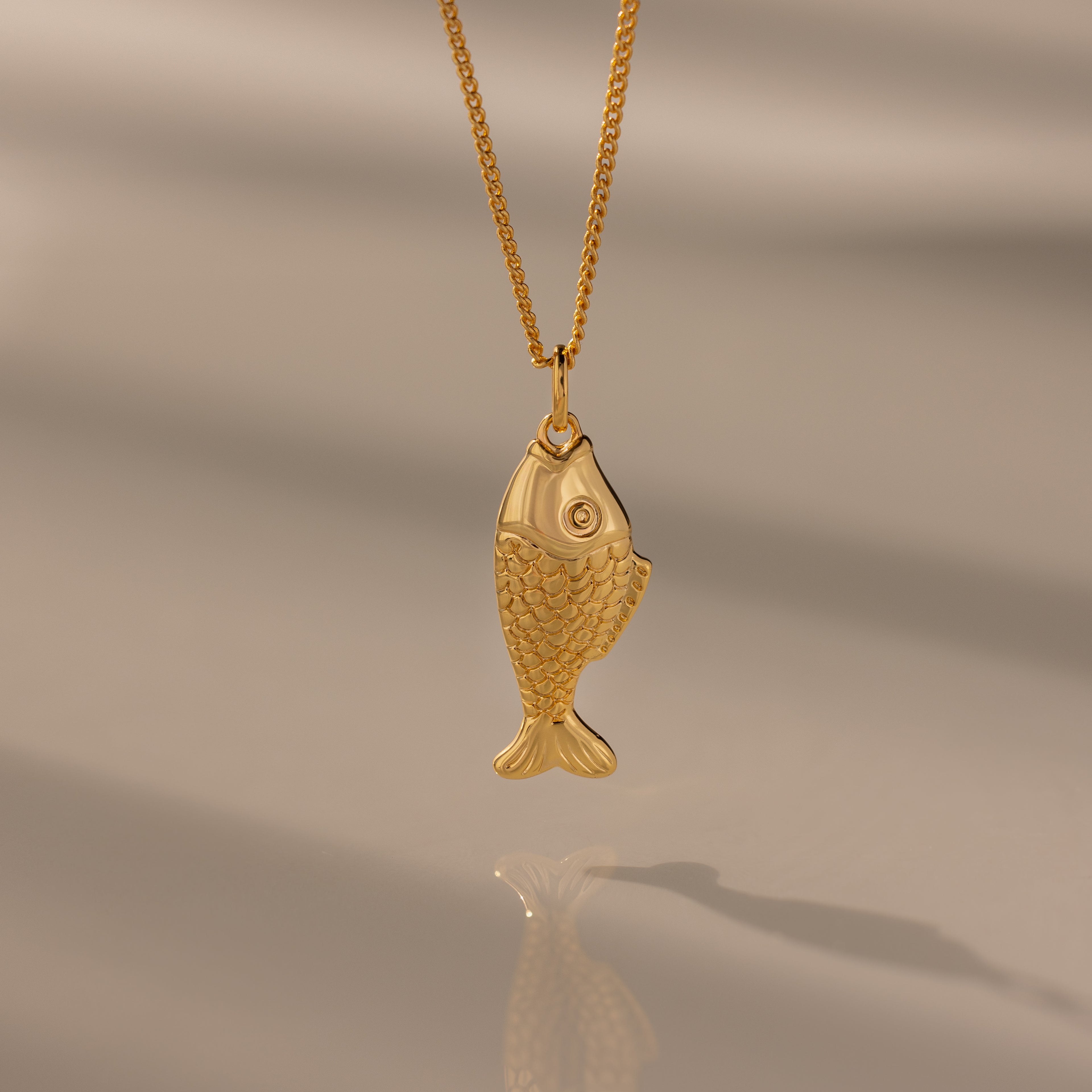 The Fish Pendant Necklace features an ocean-inspired design on a gold chain, perfect for layering and shown against a soft, neutral background.