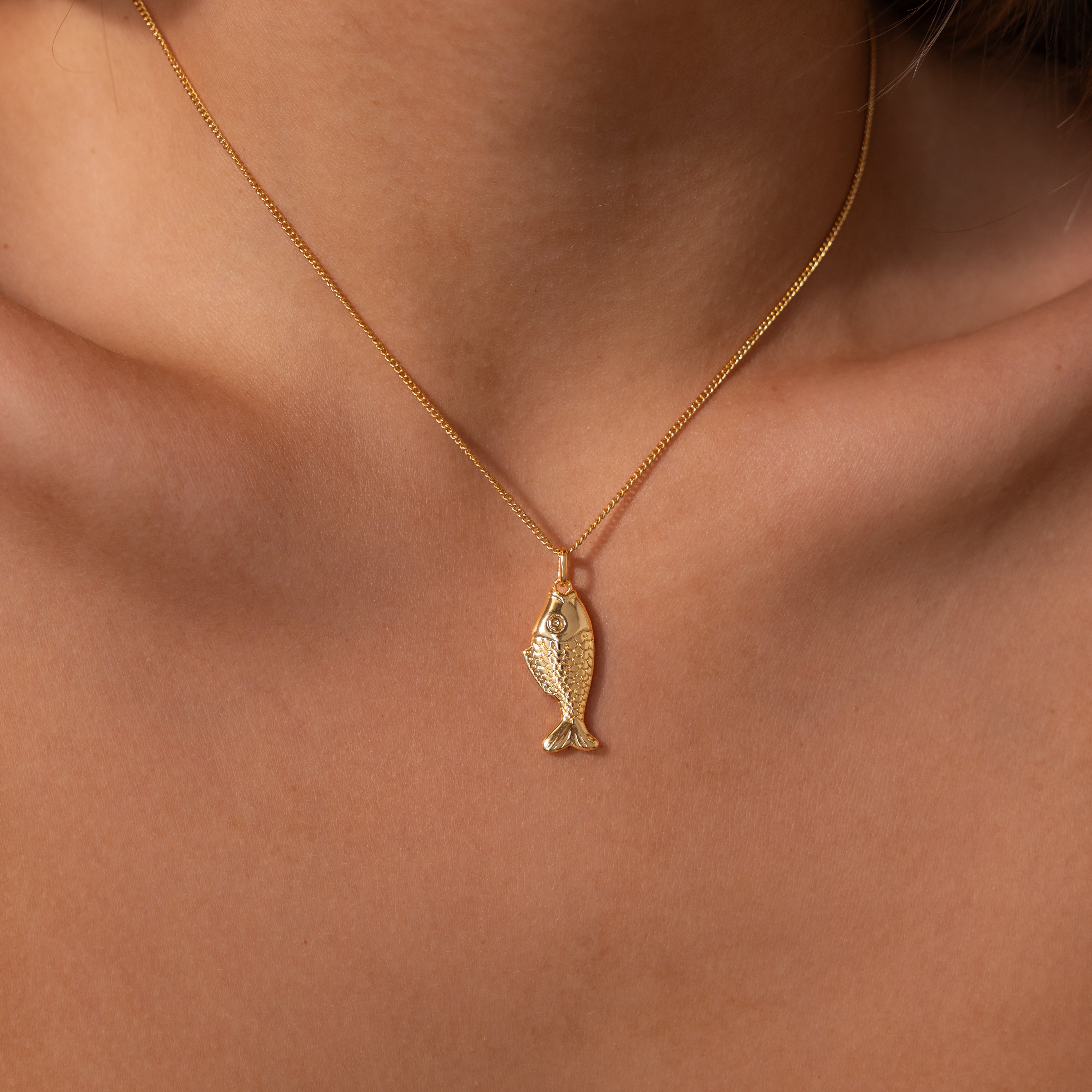 The Fish Pendant Necklace in 18K Gold, worn close to the skin, features an elegant ocean-inspired design—perfect for layering with your favorite pieces.