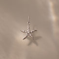 The Pave Starfish Charm in Silver is displayed on a smooth beige background with soft light reflections, highlighting the elegant coastal charm of this starfish jewelry.