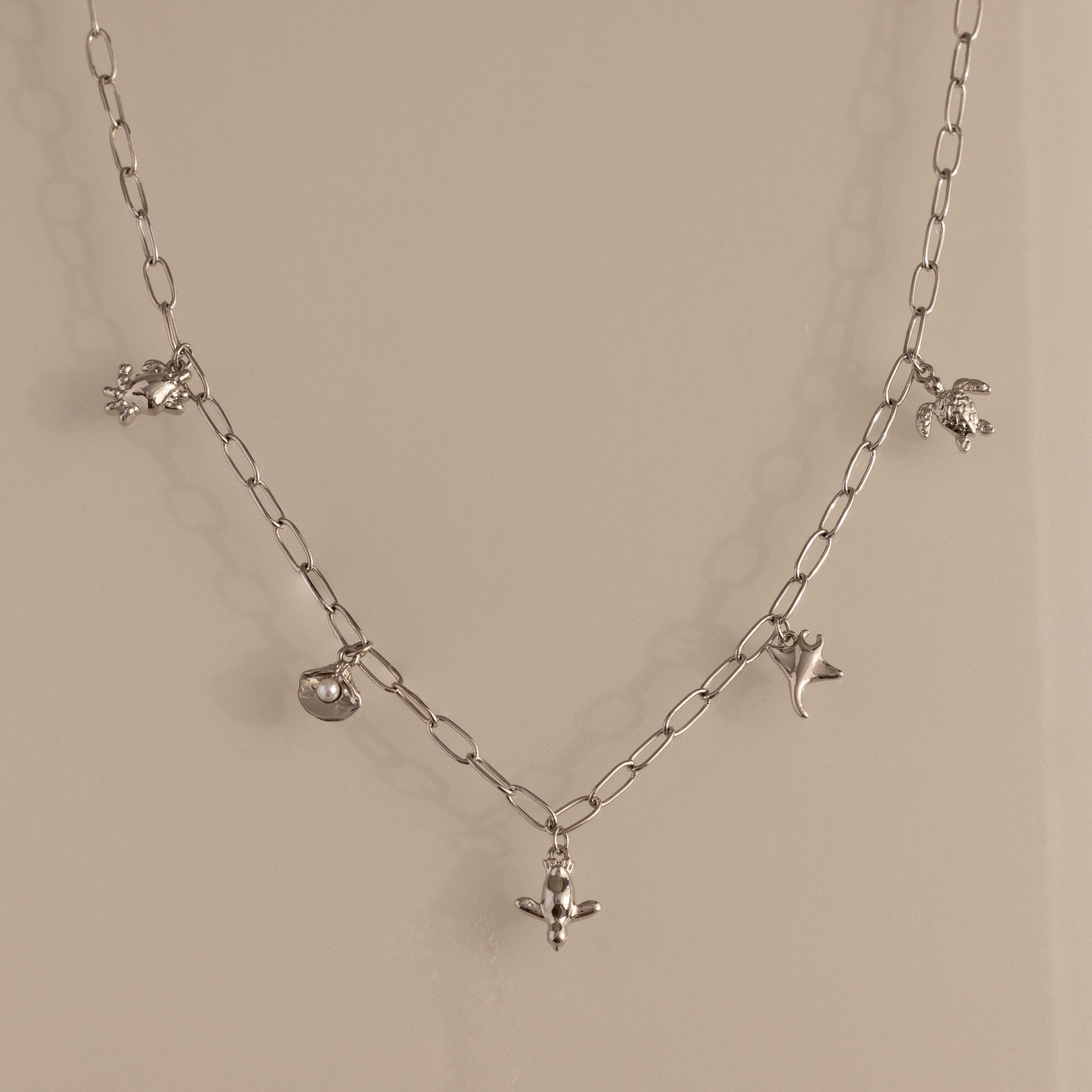 The Seaside Charm Necklace in Silver features five ocean-themed charms—crab, pufferfish, turtle, dolphin, and stingray—making it perfect beach jewelry for your summer necklace collection.