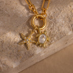The Diamond Turtle Charm in 18K Gold, featuring clear stones and a diamond-detailed shell, creates stunning ocean-inspired jewelry when paired with a gold necklace on a textured stone surface.