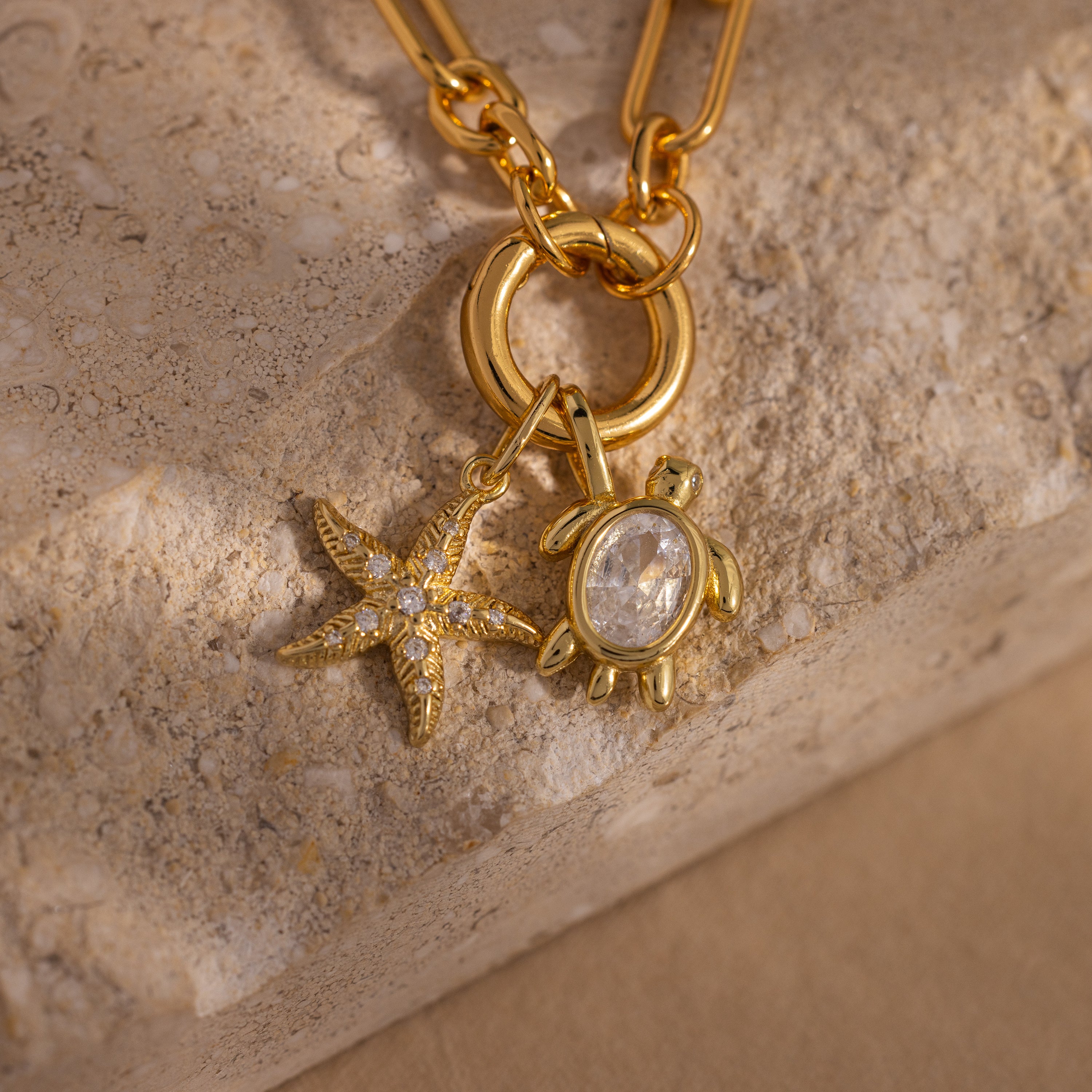 Diamond Turtle Charm: A gold necklace adorned with a diamond-studded turtle and starfish, both sparkling with gemstones, displayed on textured stone—a striking piece of ocean-inspired jewelry.