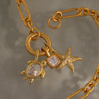 18K Gold chain featuring ocean-inspired charms: a Diamond Turtle Charm, a square gemstone, and a starfish—each adorned with sparkling clear stones.