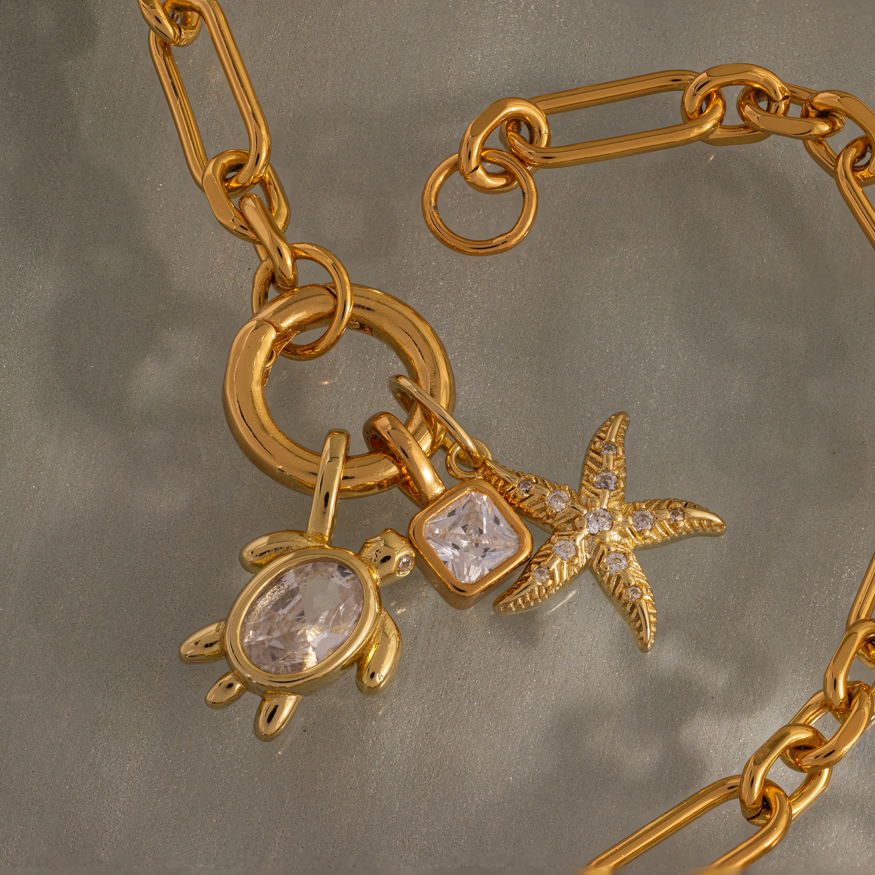 18K Gold chain featuring ocean-inspired charms: a Diamond Turtle Charm, a square gemstone, and a starfish—each adorned with sparkling clear stones.
