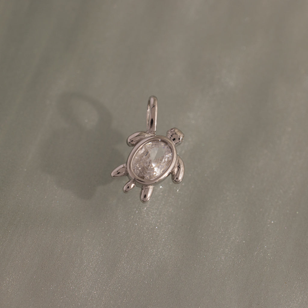 The Diamond Turtle Charm in Silver features a clear gemstone shell on a textured silver surface—an ideal piece for fans of ocean-inspired jewelry.