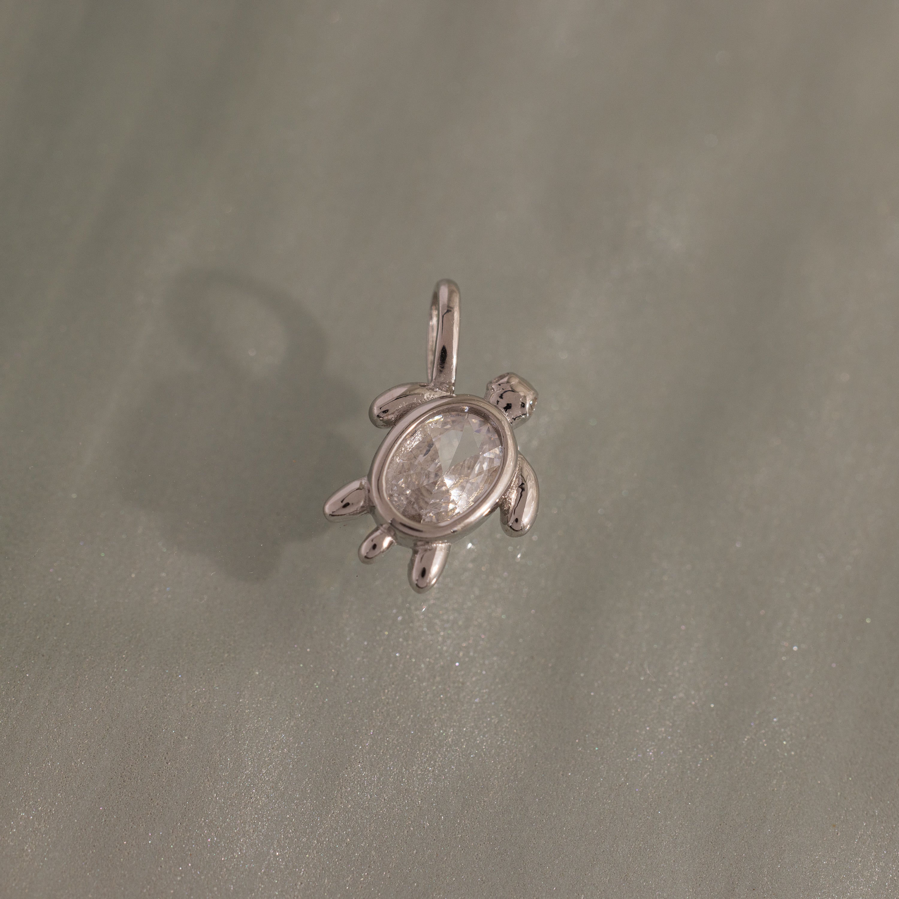 The Diamond Turtle Charm in Silver features a clear gemstone shell on a textured silver surface—an ideal piece for fans of ocean-inspired jewelry.
