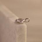The Diamond Turtle Charm features a shimmering silver finish and small gemstone, resting atop light marble to embody the beauty of ocean-inspired jewelry.
