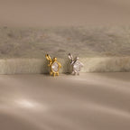 Two Diamond Turtle Charms—one gold, one silver—rest on a marble surface under soft lighting, each featuring a delicate turtle design ideal for ocean jewelry lovers.
