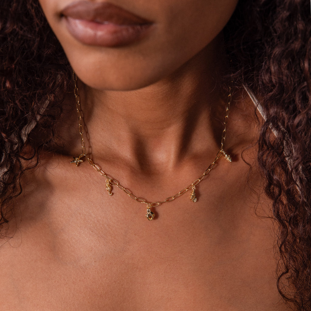 A woman wears the Ocean Charm Necklace in 18K Gold, featuring delicate charms—ideal summer jewelry for a relaxed, effortless look.
