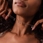 A woman holds the Ocean Charm Necklace in Silver against her neck with both hands, highlighting the beauty of seaside-inspired jewelry.