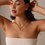 Woman in a white strapless top poses with arms raised, wearing layered gold necklaces featuring the 18K Gold Diamond Turtle Charm with a diamond-detailed shell.