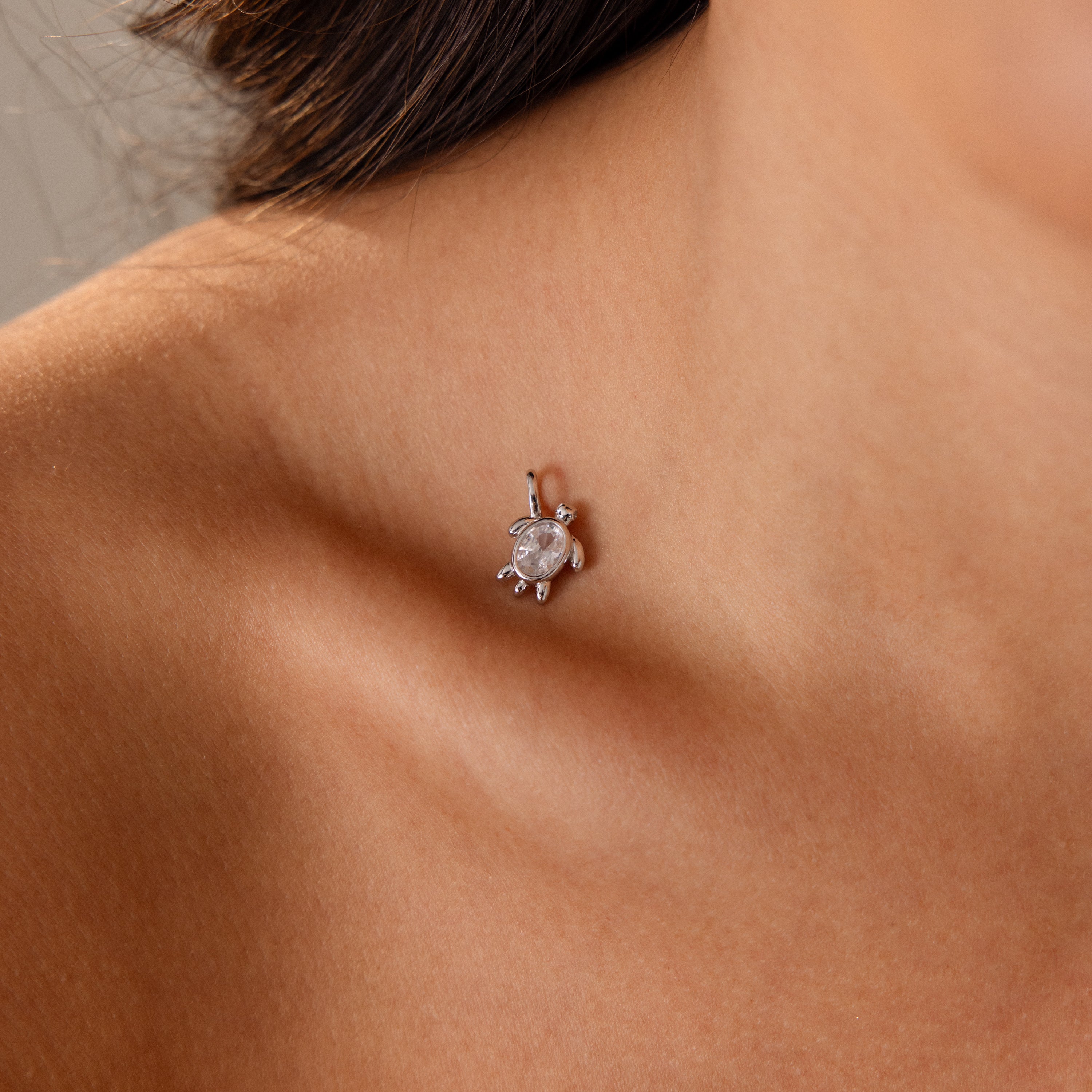 A close-up of a womans collarbone with the Diamond Turtle Charm in Silver, an ocean-inspired pendant, resting on her skin.