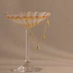 A gold charm bracelet draped over a seashell-shaped glass dish on a beige background, perfect for pairing with your favorite summer jewelry or the Ocean Charm Necklace in 18K Gold.