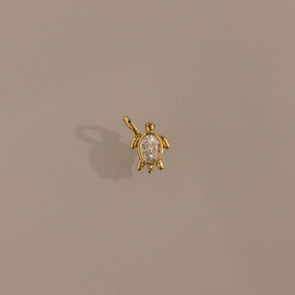 Diamond Turtle Charm in 18K Gold with a diamond-detailed shell, ocean-inspired, shown on a plain beige background.