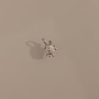 The Diamond Turtle Charm in Silver features a small turtle design with a loop, casting a shadow on beige—ideal for fans of ocean-inspired jewelry.