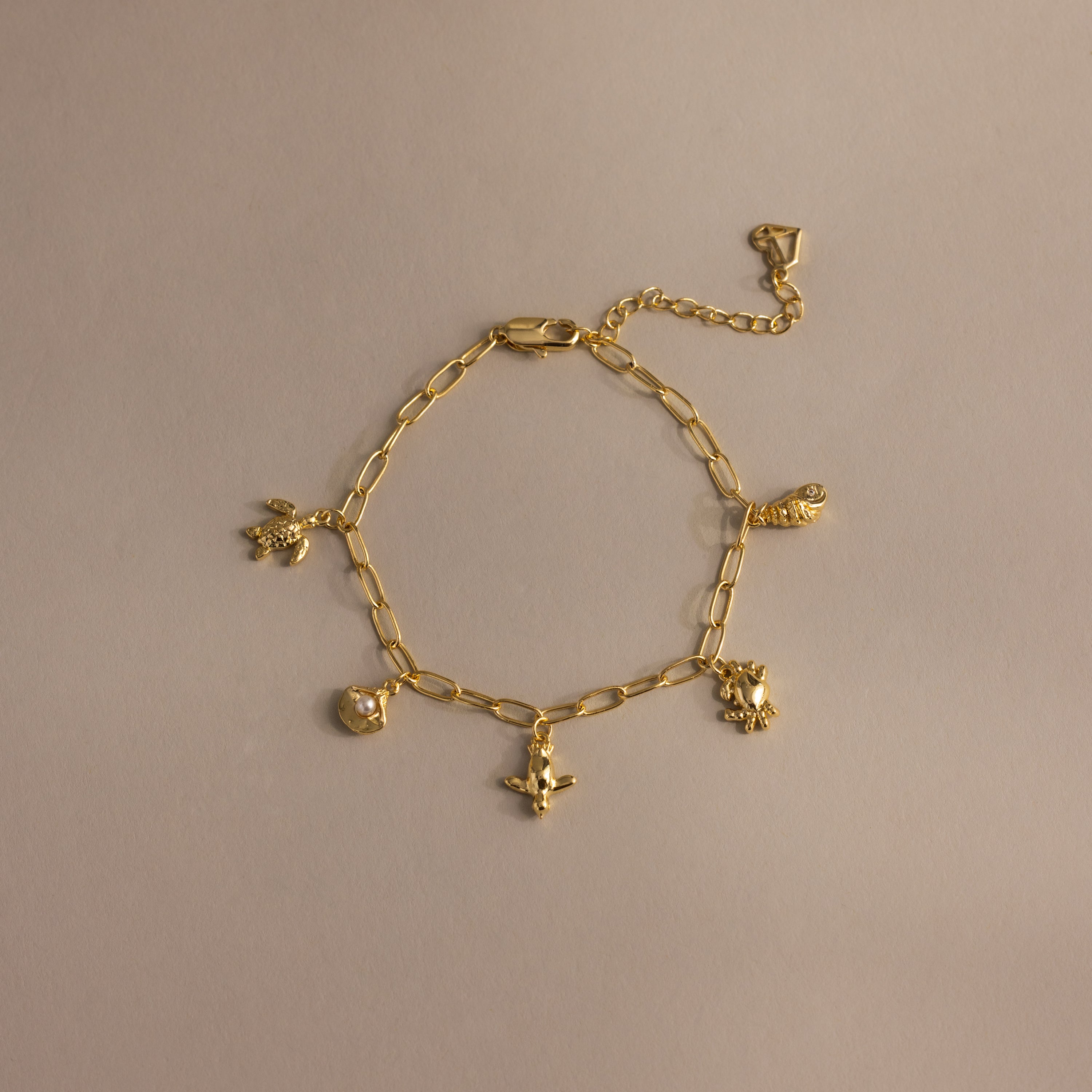 Seaside Charm Bracelet in 18K Gold with four small animal charms, ideal for coastal jewelry lovers, shown on a simple beige background.