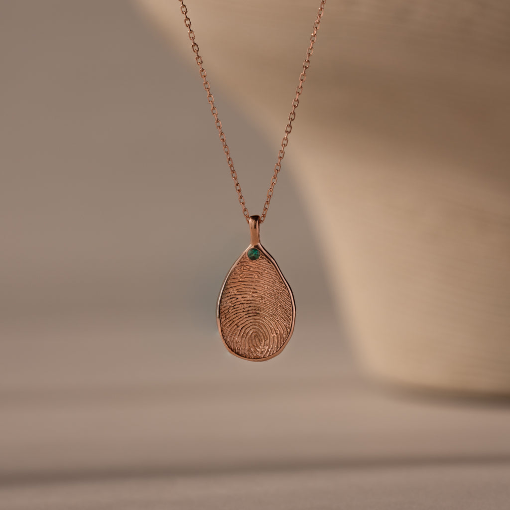 The Fingerprint Birthstone Teardrop Necklace in Rose Gold features a custom fingerprint imprint and a small green gemstone, making it a perfect personalized jewelry piece.