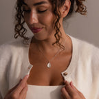 Woman smiling and looking down, wearing a white cardigan, a tank top, and the Fingerprint Birthstone Teardrop Necklace in Sterling Silver—a personalized jewelry piece that adds meaning to her look.