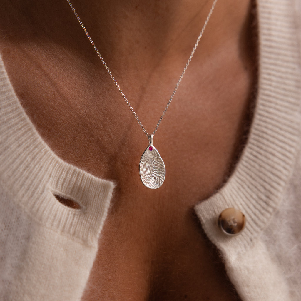 A Fingerprint Birthstone Teardrop Necklace in Sterling Silver, worn with a cream-colored knit sweater.