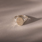 The Organic Fingerprint Signet Ring in Sterling Silver features a round bezel engraved with a fingerprint, creating a unique, personalized piece of jewelry that serves as a meaningful wearable keepsake.