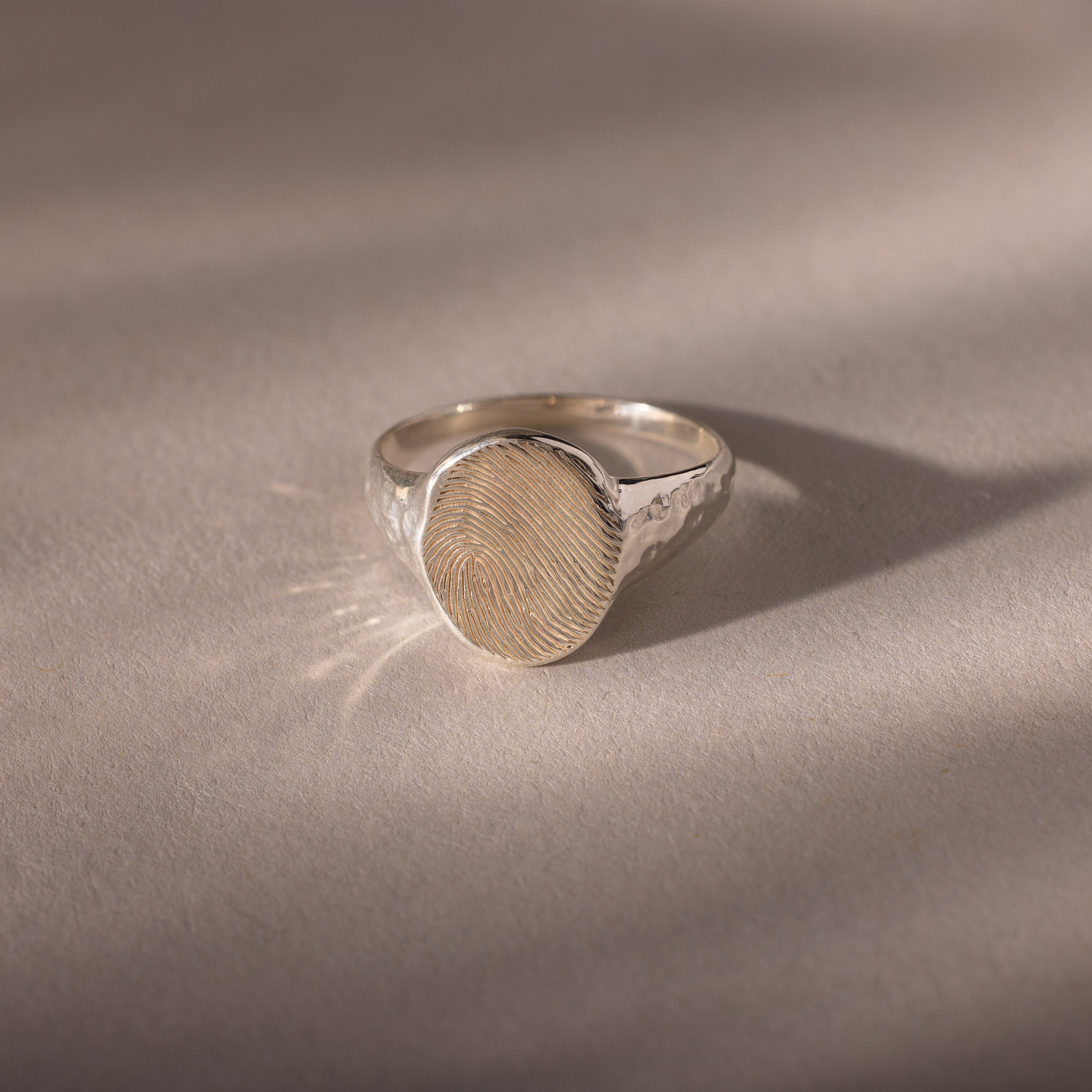 The Organic Fingerprint Signet Ring in Sterling Silver features a round bezel engraved with a fingerprint, creating a unique, personalized piece of jewelry that serves as a meaningful wearable keepsake.