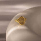 The Organic Fingerprint Signet Ring in 18K Gold is a personalized jewelry piece, showcased on a smooth, ivory-colored surface.