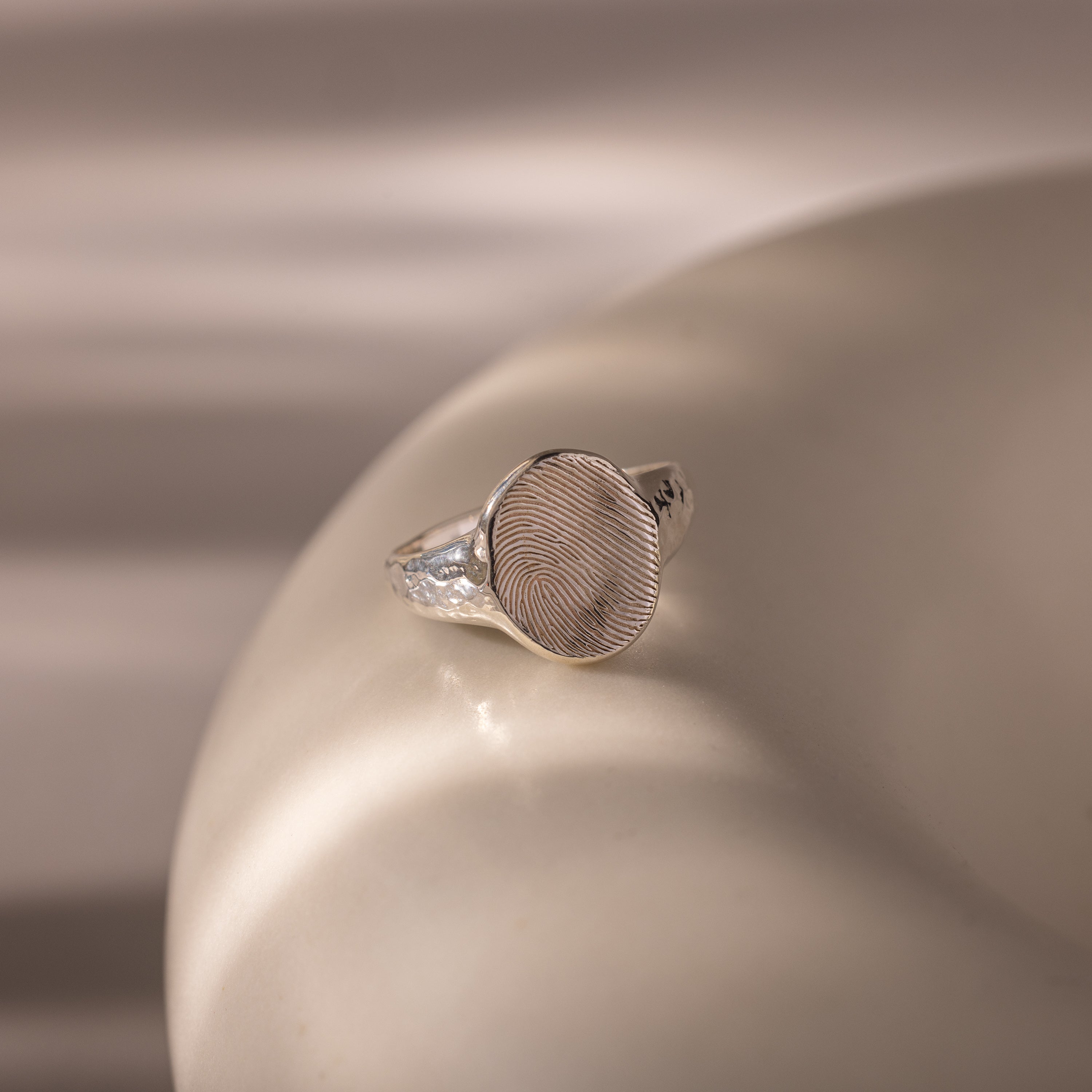 The Organic Fingerprint Signet Ring in Sterling Silver, featuring a round engraved top, rests on a smooth, light surface—a timeless, personalized jewelry piece.