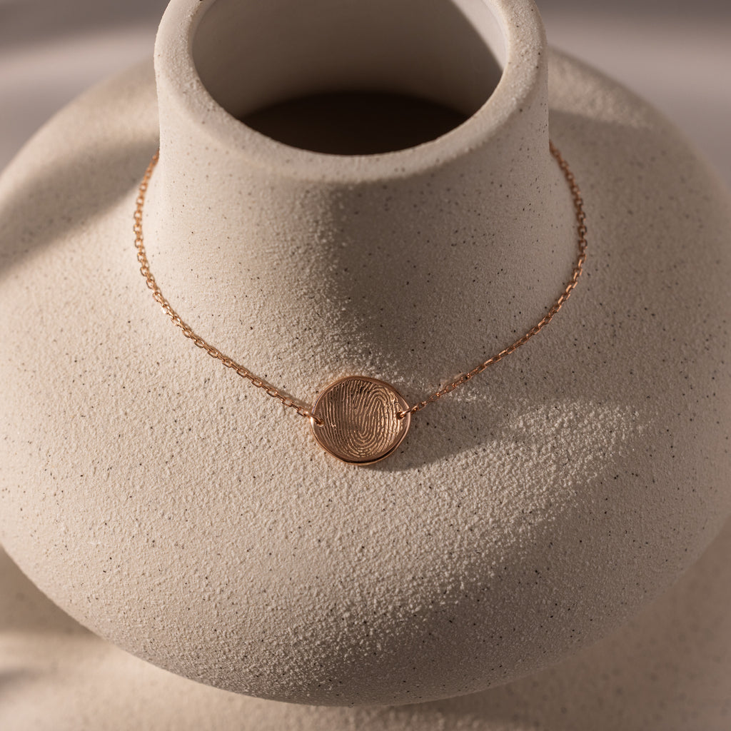 A dainty rose gold bracelet with an organic fingerprint charm, displayed on a textured white bust—an elegant piece of memorial jewelry and the perfect personalized gift.