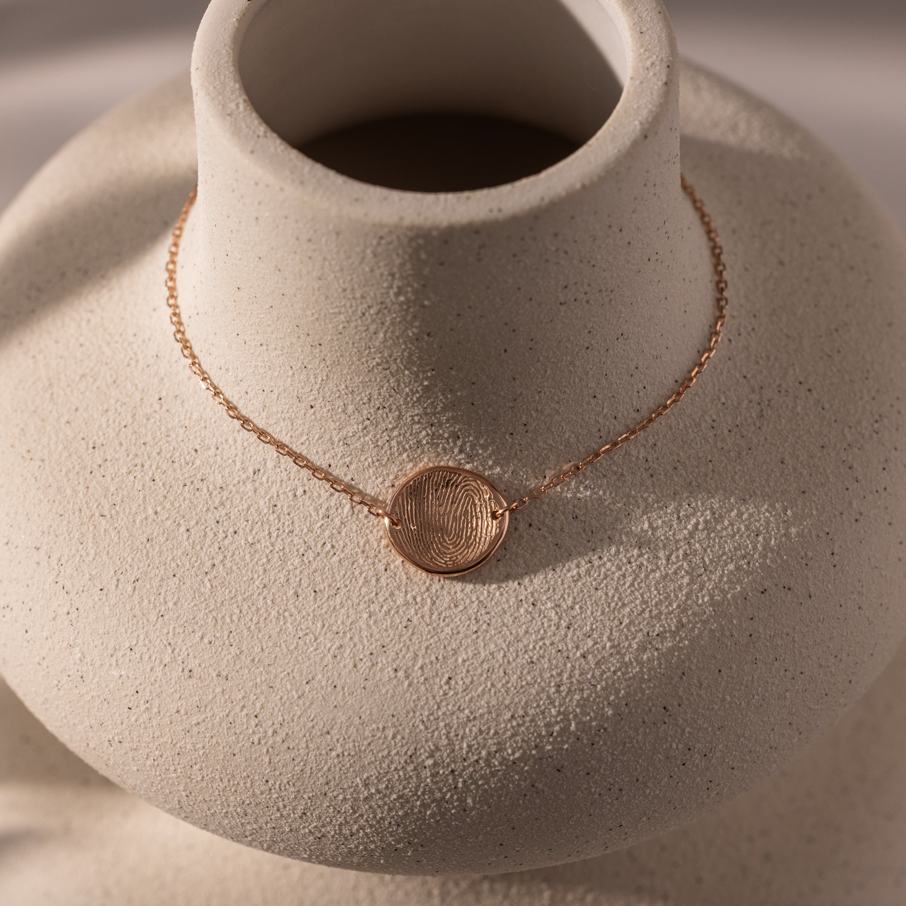 A dainty rose gold bracelet with an organic fingerprint charm, displayed on a textured white bust—an elegant piece of memorial jewelry and the perfect personalized gift.