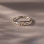 The Hand & Footprint Signet Ring in Sterling Silver features tiny engraved hand and footprints on a polished surface—ideal as a cherished baby keepsake, beautifully displayed on a light background.
