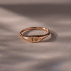 The Hand & Footprint Signet Ring in Rose Gold, engraved with tiny baby footprints, rests on a smooth, neutral surface—a perfect keepsake.
