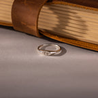 The Hand & Footprint Signet Ring in Sterling Silver sits on a gray surface beside a leather-bound book—a timeless baby keepsake to treasure special memories.