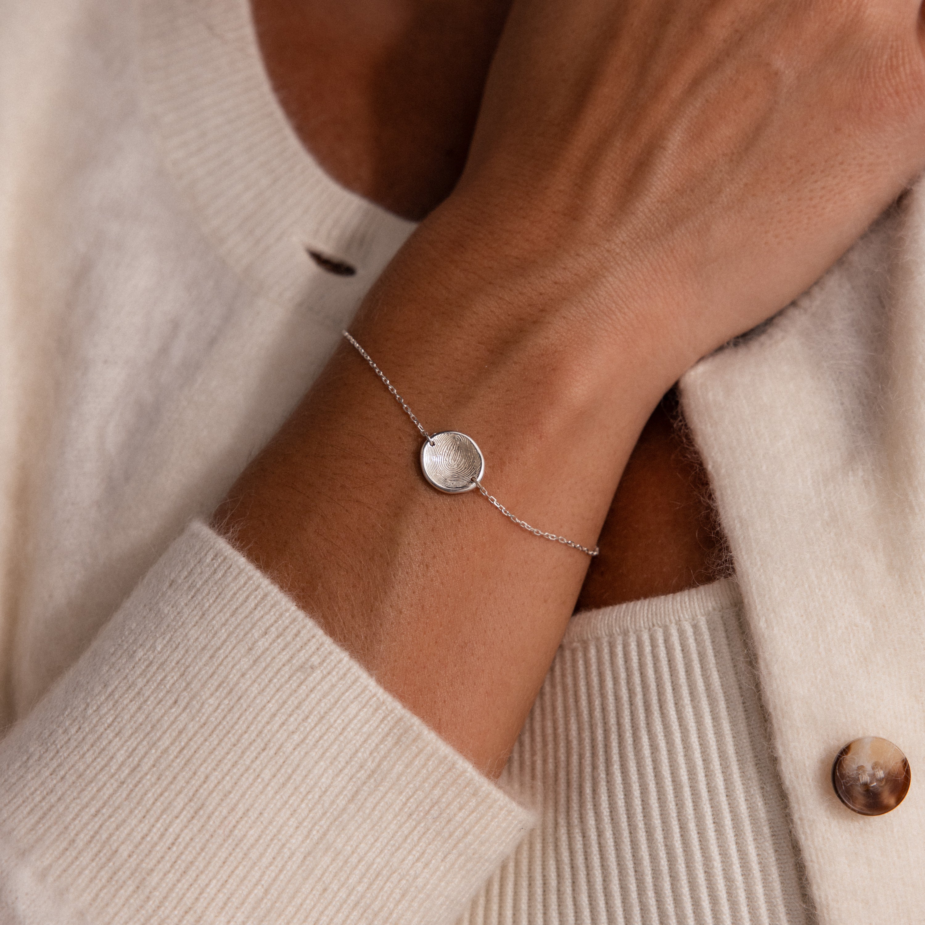 A close-up of the Dainty Organic Fingerprint Bracelet in Sterling Silver on a wrist with a cream cardigan—a unique piece of personalized jewelry.