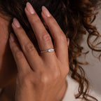 A hand with manicured nails wears the Hand & Footprint Signet Ring in Sterling Silver next to curly brown hair.