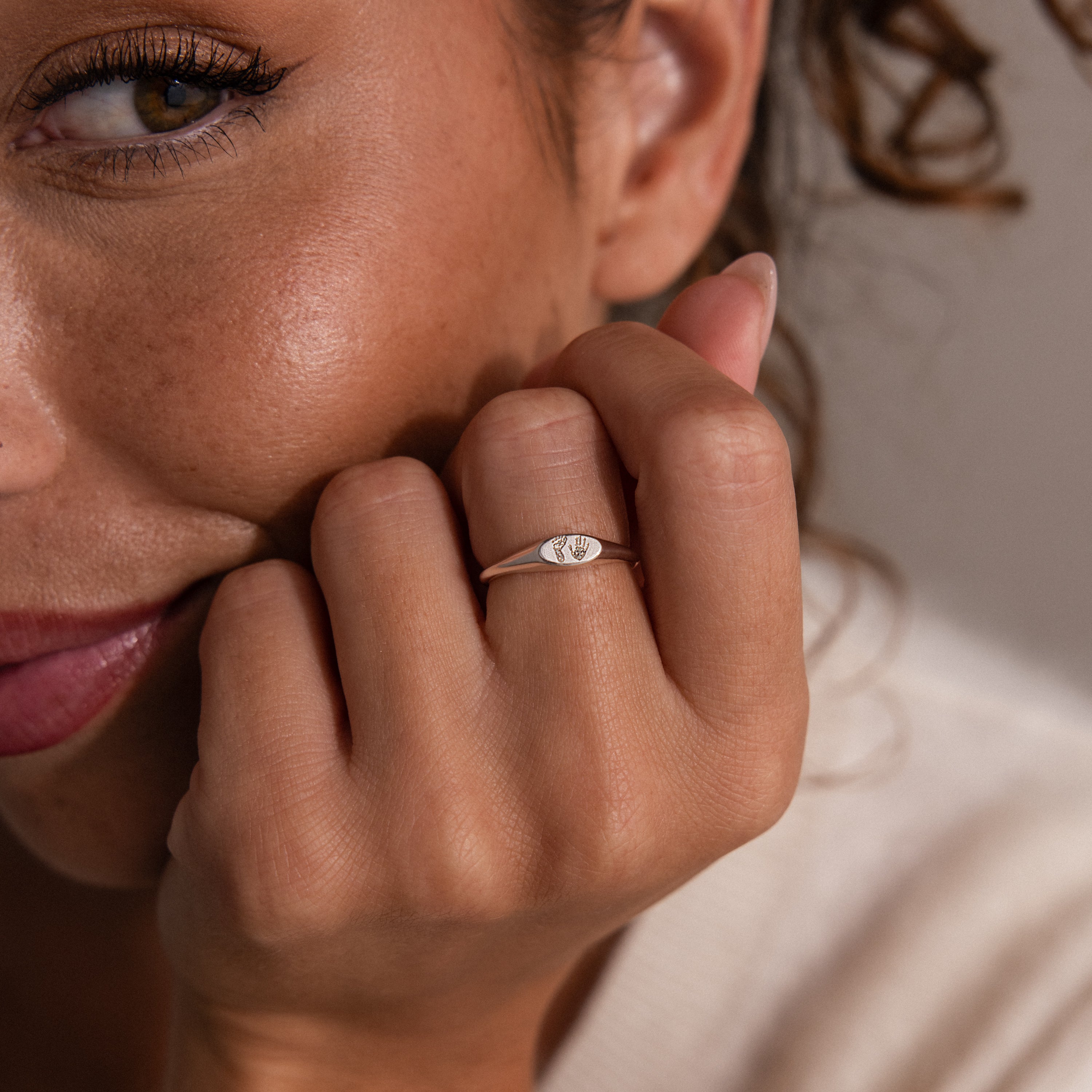 A woman smiles softly, displaying the Hand & Footprint Signet Ring with its engraved design—a timeless keepsake jewelry piece.