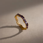 The Staggered Marquise Amethyst Ring casts a delicate shadow on a beige surface, its small purple gemstones sparkling softly.