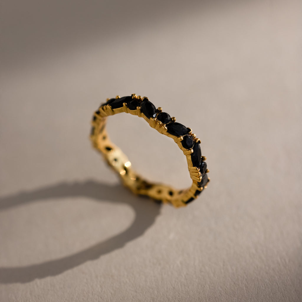The Staggered Marquise Onyx Ring with black gemstones casts a shadow on a light, textured surface.