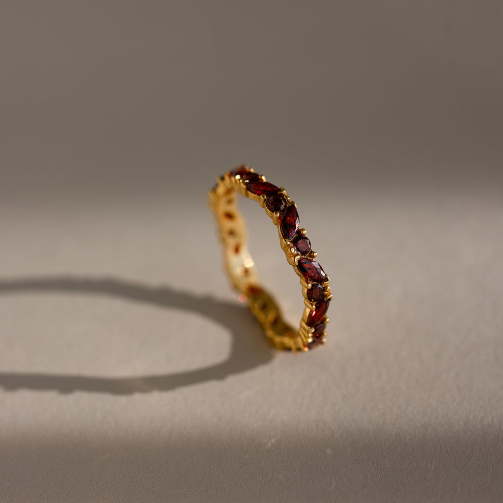 The Staggered Marquise Garnet Ring shines with red gemstones, casting a shadow on a softly lit neutral surface.