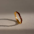 The Staggered Marquise Garnet Ring shines with red gemstones, casting a shadow on a softly lit neutral surface.