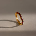 The Staggered Marquise Garnet Ring shines with red gemstones, casting a shadow on a softly lit neutral surface.