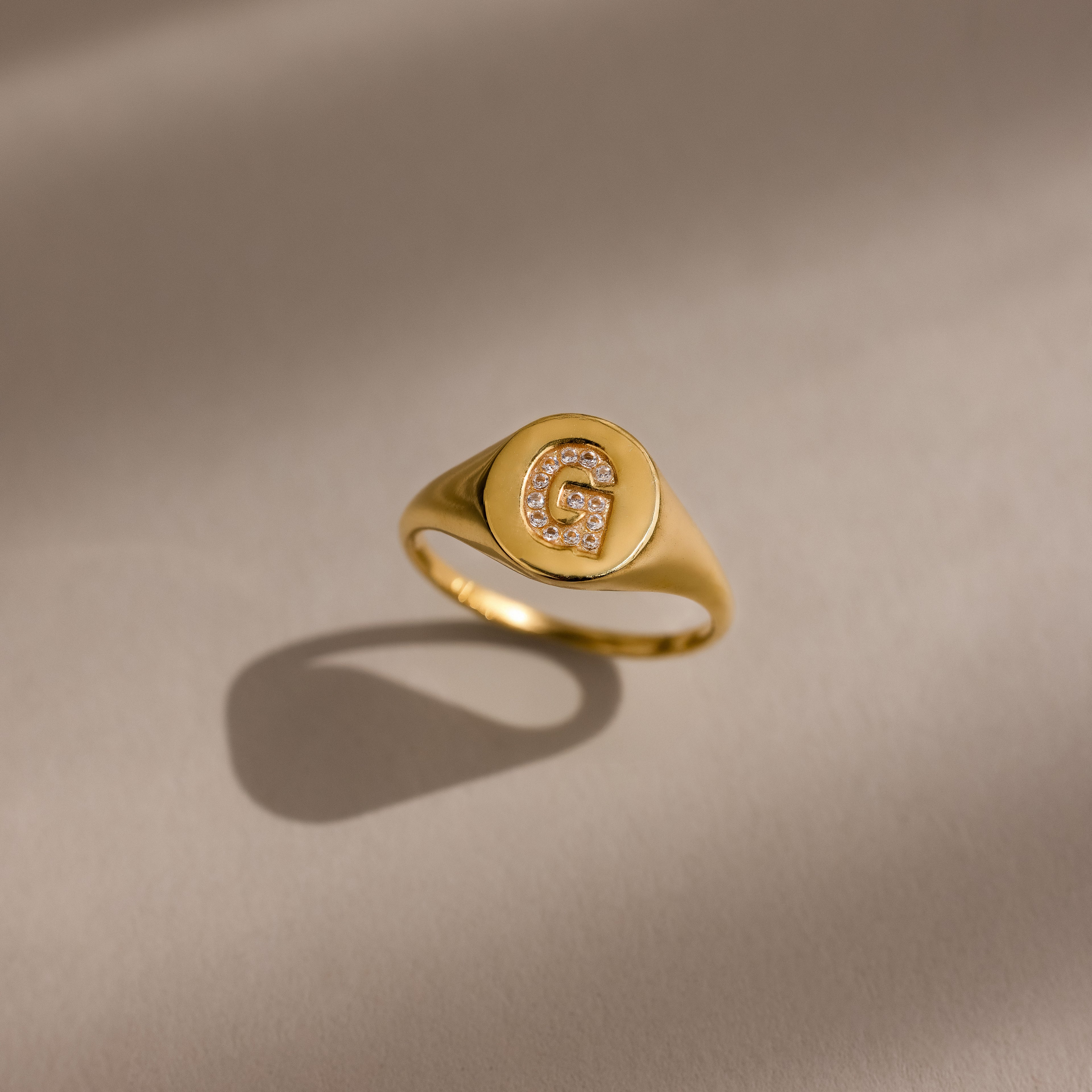The Pave Initial Signet Ring in 18K Gold features a crystal-studded initial G that sparkles with small diamonds on a neutral background, making it the perfect statement ring.