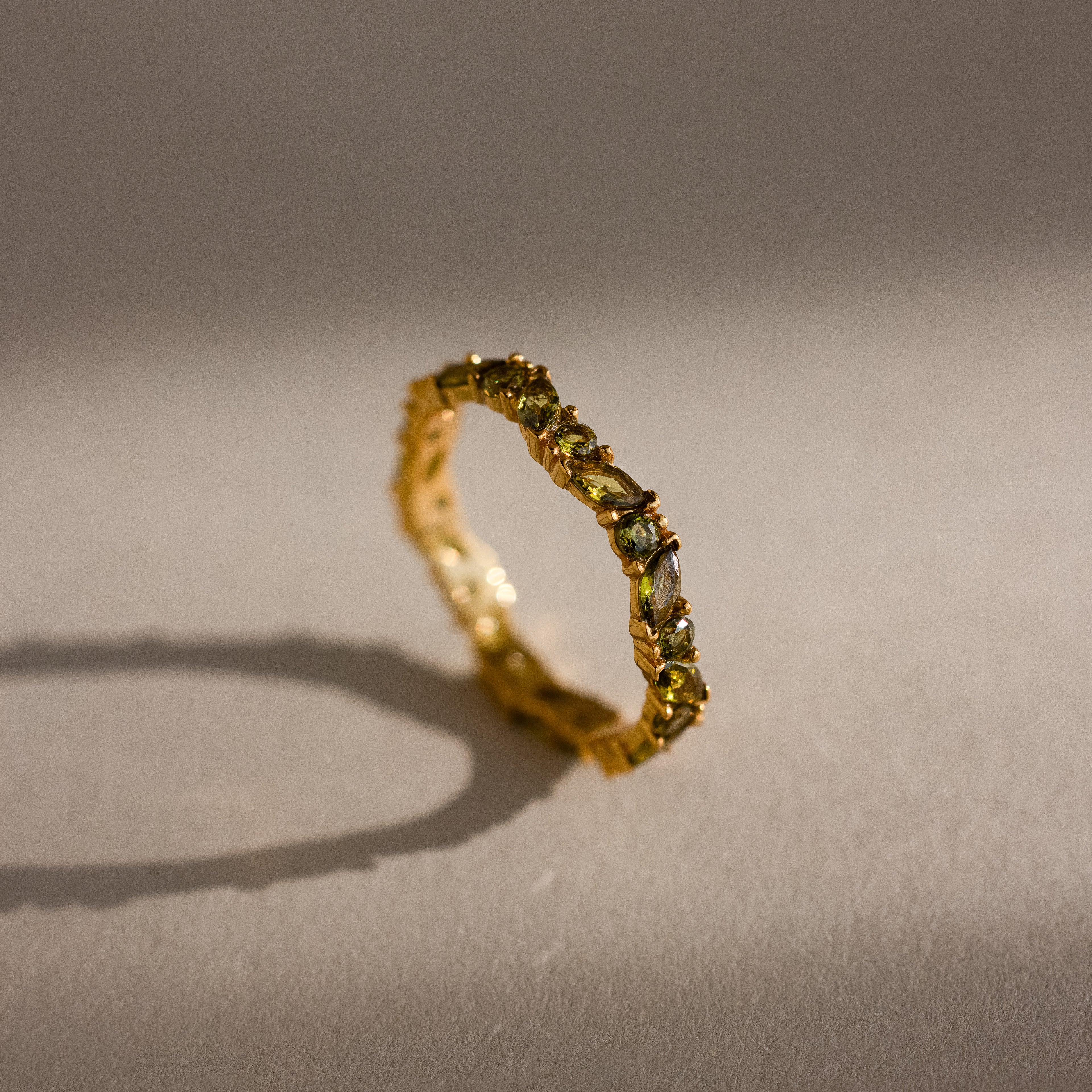 The Staggered Marquise Peridot Ring casts a shadow on a neutral, softly lit surface.