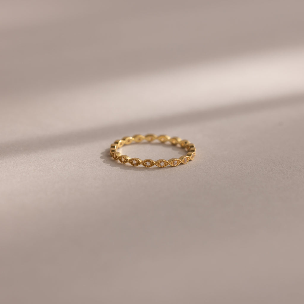The Dainty Marquise Diamond Ring, featuring a twisted gold band, rests on a smooth beige surface beneath soft light, evoking timeless Art Deco elegance.