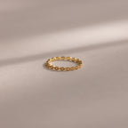 The Dainty Marquise Diamond Ring, featuring a twisted gold band, rests on a smooth beige surface beneath soft light, evoking timeless Art Deco elegance.