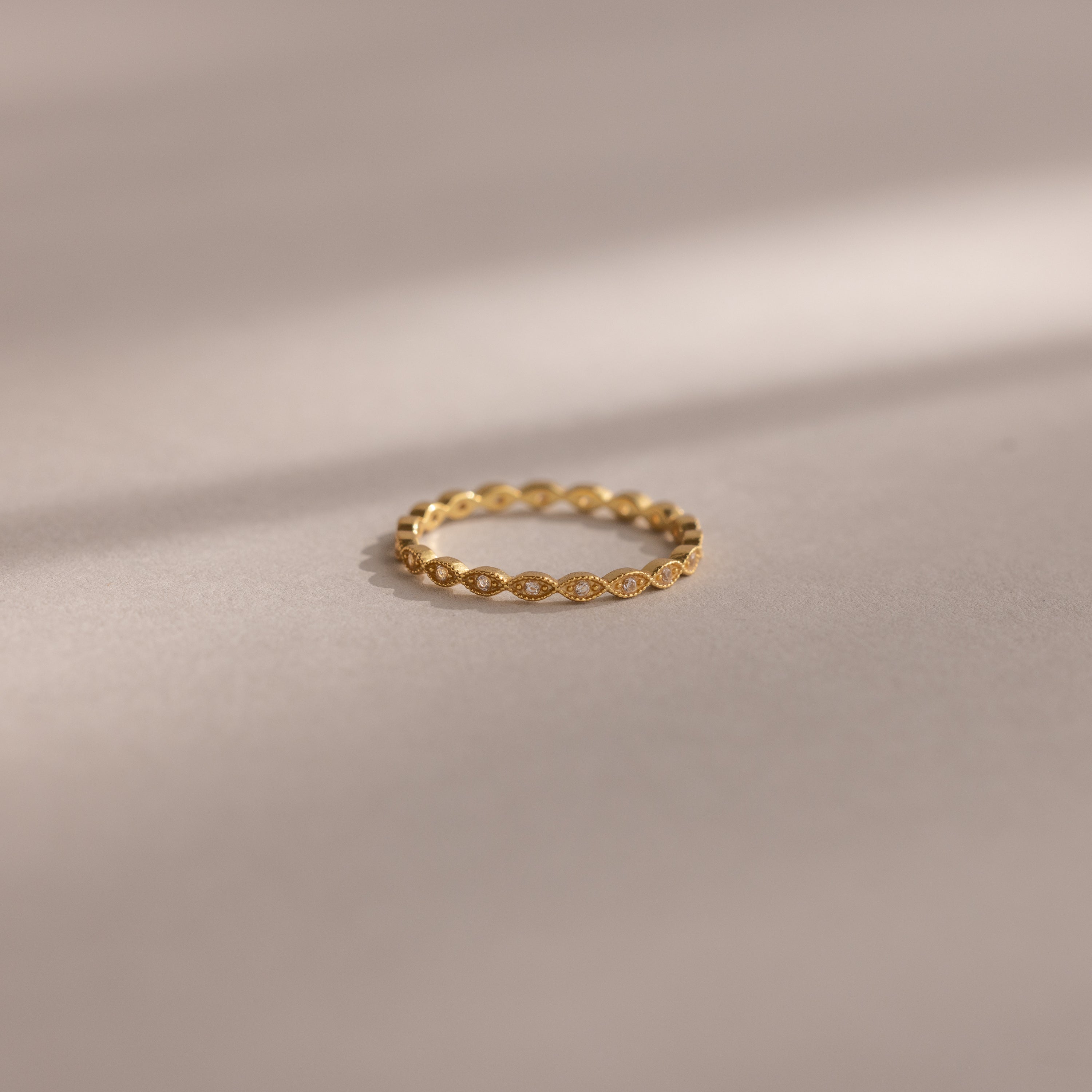 The Dainty Marquise Diamond Ring, featuring a twisted gold band, rests on a smooth beige surface beneath soft light, evoking timeless Art Deco elegance.