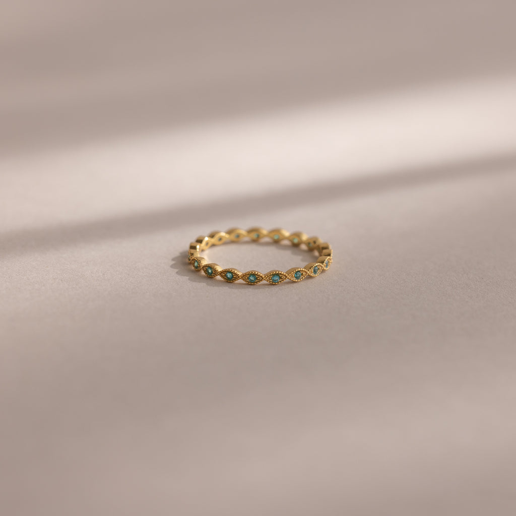 The Dainty Marquise Blue Zircon Ring, a delicate Art Deco-inspired gold piece with a shimmering blue zircon, rests on a soft beige surface with gentle shadow lines.