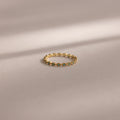 The Dainty Marquise Blue Zircon Ring, a delicate Art Deco-inspired gold piece with a shimmering blue zircon, rests on a soft beige surface with gentle shadow lines.
